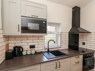 A kitchen counter with a microwave, kettle, toaster, three canisters, sink, stove, oven and extractor hood at Top Holme Cottage in Newbald