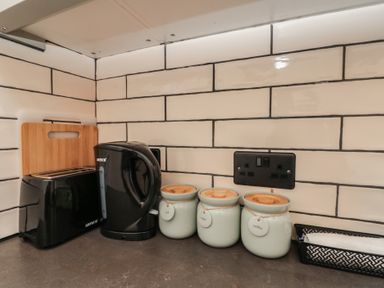 A kitchen countertop with a black toaster a black kettle three labeled jars and a tray with a towel at Top Holme Cottage in Newbald