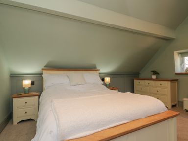 A bedroom with a bed in the center two bedside tables with lamps and a dresser with a plant at Top Holme Cottage in Newbald