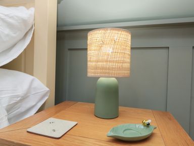 A bedside table with a green lamp a coaster and a green leaf-shaped dish with a bee decoration at Top Holme Cottage in Newbald