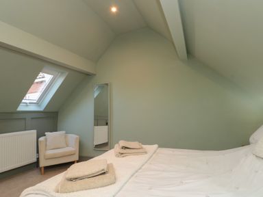 A bedroom with a bed towels armchair and wall mirror at Top Holme Cottage in Newbald
