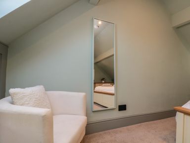 A white armchair with a cushion next to a wall mirror in a room at Top Holme Cottage in Newbald