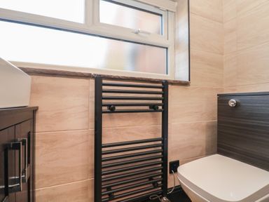 A bathroom with a black towel radiator under a frosted window a white toilet next to a dark wood cabinet at Top Holme Cottage in Newbald