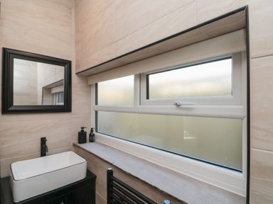 A bathroom with a rectangular sink black faucet soap dispensers window with frosted glass and a black framed mirror at Top Holme Cottage in Newbald