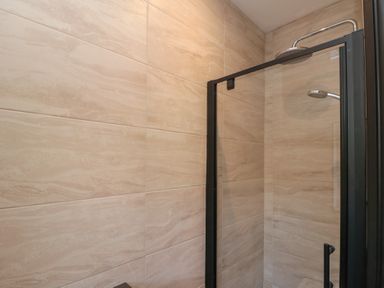 A tiled shower cubicle with a glass door and dual shower heads at Top Holme Cottage in Newbald
