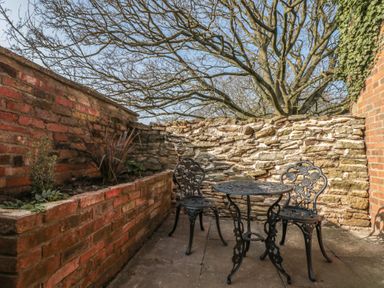 An outdoor patio area with two metal chairs and a round table next to brick and stone walls at Top Holme Cottage in Newbald