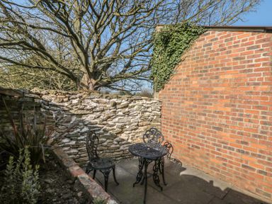A small outdoor patio with a round metal table and two chairs beside a stone and brick wall at Top Holme Cottage in Newbald