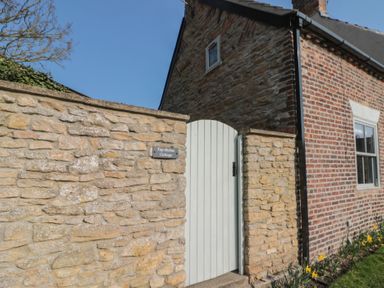 An exterior stone wall with a white wooden gate next to a brick house at Top Holme Cottage in Newbald