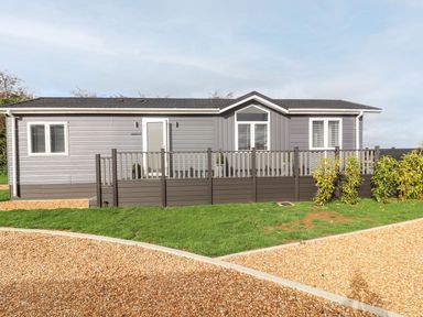 A single story grey house with white trim a front porch with railing and a gravel driveway at The Gallops in Chipping Norton