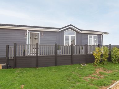 A grey house with a porch and railing in front with grass and plants at The Gallops in Chipping Norton