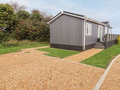 A gray modular home with gravel pathways and grass patches with trees in the background at The Gallops in Chipping Norton