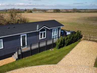 A black mobile home with a small porch and steps in front of open fields at The Gallops in Chipping Norton
