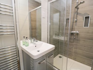 A bathroom with a sink, mirror, towel warmers, and a glass shower enclosure with a showerhead at The Gallops in Chipping Norton