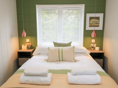 A bedroom with a bed with pillows and folded towels on it and nightstands with lamps and decor at The Gallops in Chipping Norton