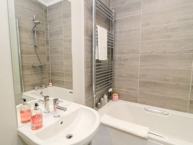 A bathroom with a white sink and faucet a bathtub with candles and towel and tiled walls at The Gallops in Chipping Norton