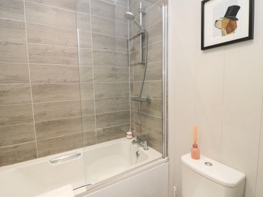 A bathroom with a bathtub and shower combination and a toilet with a reed diffuser on the cistern at The Gallops in Chipping Norton