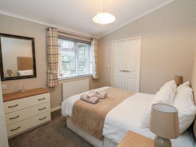A bedroom with a double bed bedside lamps a chest of drawers and a window with curtains at Lodge 2 in Auchterarder