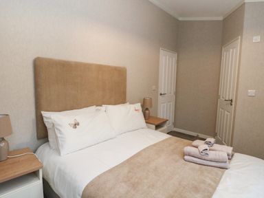 A bedroom with a bed with beige headboard pillows and folded towels on bed at Lodge 2 in Auchterarder
