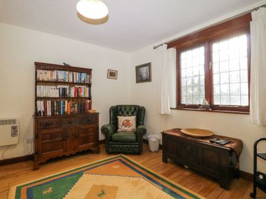A room with a wooden bookshelf filled with books an armchair a wooden chest under a window and a patterned rug on the floor at Wringford Farm Annexe Rame near Kingsand