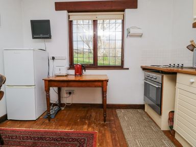 A kitchen with a wooden table holding a kettle and toaster a white refrigerator an oven under a countertop and a window with a view at Wringford Farm Annexe in Rame near Kingsand