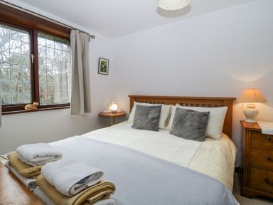 A bedroom with a double bed two grey pillows bedside tables lamps and towels on the foot of the bed at Wringford Farm Annexe in Rame near Kingsand