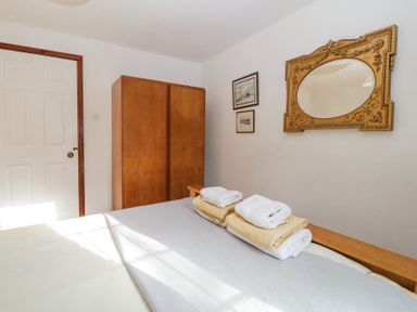 A bedroom with a wooden wardrobe a bed with folded towels and an ornate wall mirror at Wringford Farm Annexe in Rame near Kingsand