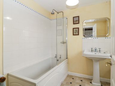 A bathroom with a bathtub and shower next to a sink with a mirror and two framed pictures on the wall at Wringford Farm Annexe Rame near Kingsand