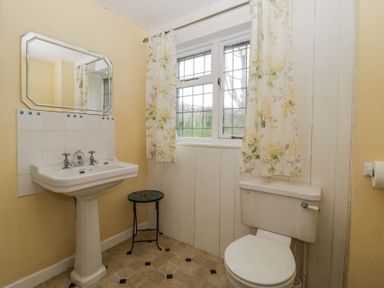 A bathroom with a pedestal sink mirror window with floral curtains small stool and a toilet at Wringford Farm Annexe Rame near Kingsand