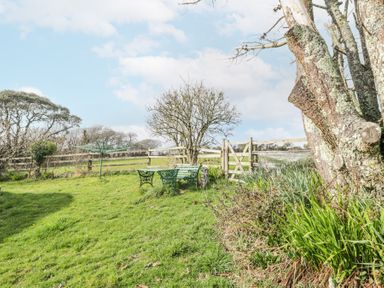 A garden with a green metal table and benches near a wooden fence and gate at Wringford Farm Annexe in Rame near Kingsand
