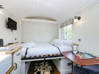 A small bedroom with a bed, a wall-mounted TV, a wooden table with magazines, and a window with a Roman blind at Airlie Burnside near Forfar