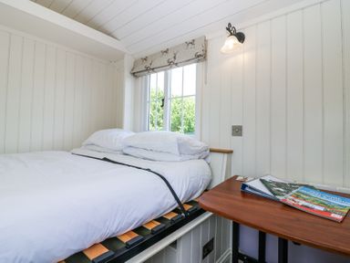 A small bedroom with a white bed and pillows next to a window with deer patterned blind and a wooden table with magazines at Airlie Burnside near Forfar