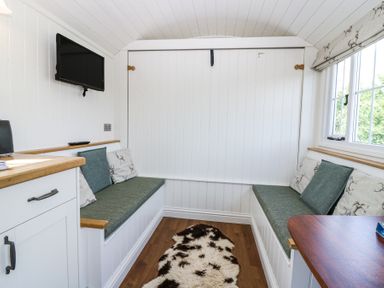 A small room with two green cushioned benches, white paneled walls, a mounted TV, and a window with patterned blinds at Airlie Burnside near Forfar
