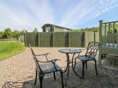 An outdoor patio with a metal table and two chairs on a circular stone platform surrounded by gravel and a green wooden fence at Airlie Burnside near Forfar