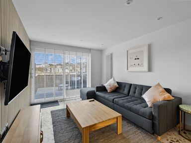 A living room with a gray sofa and wooden coffee table facing a wall-mounted TV at 5 Mermaid Court in Newquay