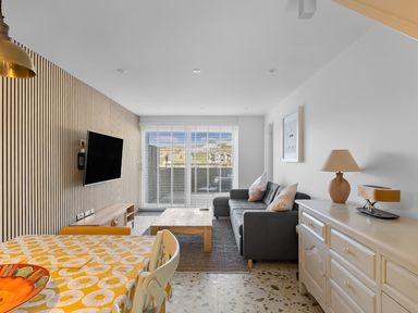 A living room with a sofa a coffee table a mounted TV and a dining table with chairs at 5 Mermaid Court in Newquay