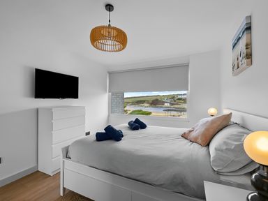 A bedroom with a bed and rolled towels next to a window showing a coastal view at 5 Mermaid Court in Newquay