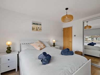 A bedroom with a white bed and blue towels on it bedside tables with lamps and a wooden door at 5 Mermaid Court in Newquay