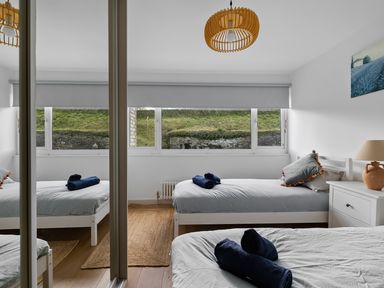 A bedroom with two single beds a bedside table with a lamp and a window with a roller blind at 5 Mermaid Court in Newquay