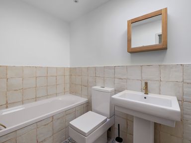 A bathroom with a bathtub toilet pedestal sink mirror and tiled walls at 5 Mermaid Court in Newquay
