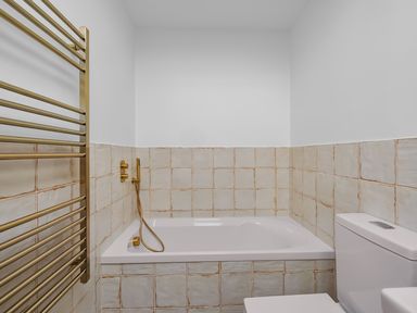 A bathroom with a bathtub, gold faucet, tiled walls, a white toilet, and a gold towel rack at 5 Mermaid Court in Newquay