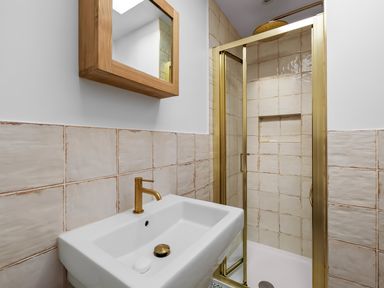 A bathroom with a white sink gold faucet a wooden framed mirror and a shower with gold frame at 5 Mermaid Court in Newquay