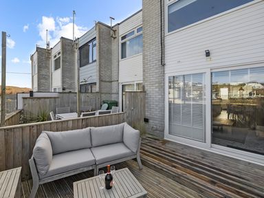 An outdoor wooden deck with a cushioned sofa and a table with a bottle and glasses at 5 Mermaid Court in Newquay