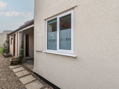 Exterior view of a building with a window displaying Priory Barn and a gravel path leading to a covered entrance at Priory Barn Apartment in Walton near Street