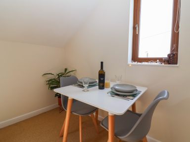 A small dining area with a white table set for two with grey chairs and a window with decorations at Priory Barn Apartment in Walton near Street