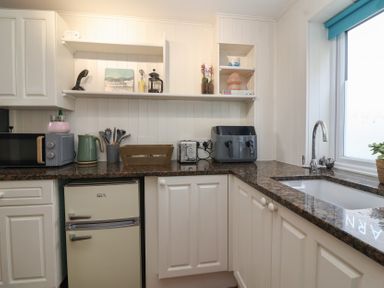 A kitchen with white cabinets a brown countertop a small refrigerator microwave kettle toaster and sink at Priory Barn Apartment Walton near Street