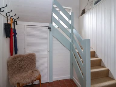 A staircase with beige carpet beside a chair with a furry seat cover and umbrellas hanging on wall hooks at Priory Barn Apartment in Walton near Street