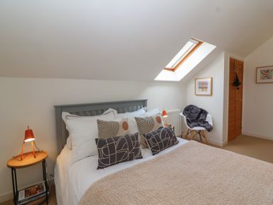A bedroom with a bed with multiple pillows bedside tables with lamps a chair with a throw a skylight window and framed artwork at Priory Barn Apartment Walton near Street