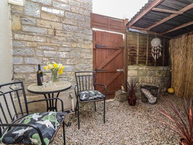 A small outdoor seating area with two chairs and a round table with flowers and a bottle at Priory Barn Apartment Walton near Street