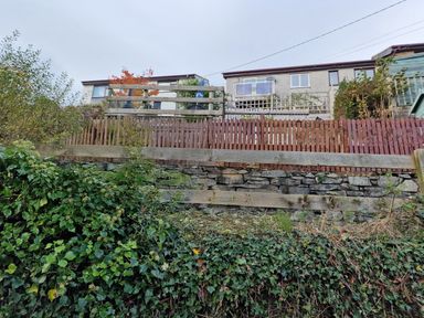 A garden with a stone wall and a wooden fence at Golygfa in Abergele