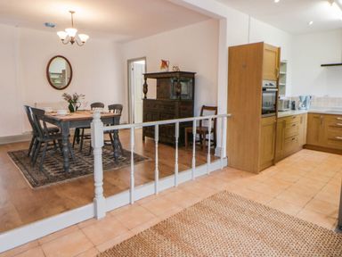 A dining room with a table and chairs leading to a kitchen at Llain in Cardigan